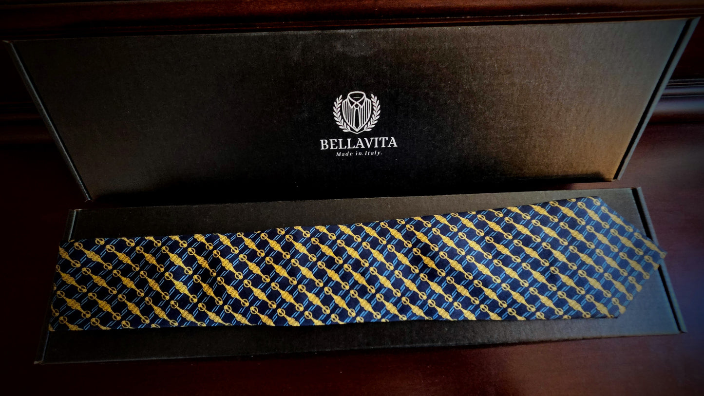 A Bellavita necktie with a blue and yellow geometric pattern, presented inside its black branded gift box on a dark wooden surface.