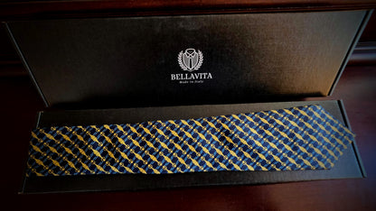 A Bellavita necktie with a blue and yellow geometric pattern, presented inside its black branded gift box on a dark wooden surface.