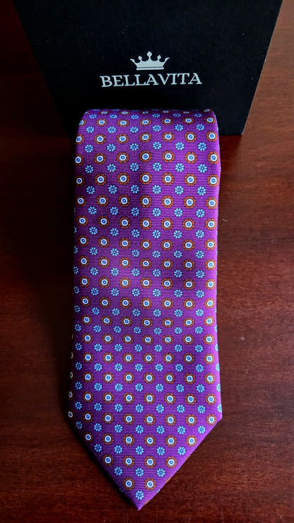 A purple silk necktie with a small multicolor floral pattern, displayed in front of its black Bellavita gift box on a dark wooden surface.